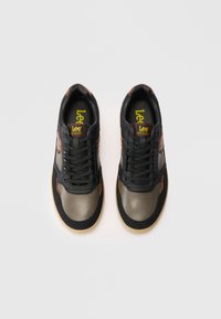 Un paio di sneaker Lee nere e marroni con lacci neri e suole beige viste dall'alto su uno sfondo bianco.