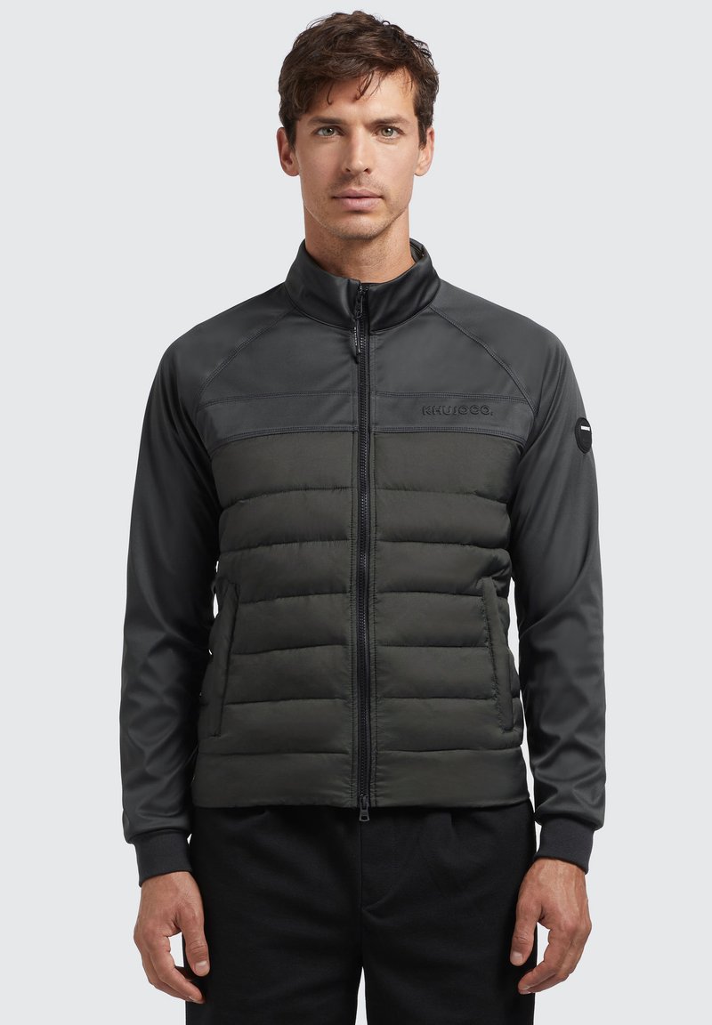 Padded jacket with a zip-front in dark gray and black. Features a smooth upper section and quilted lower section. Ribbed cuffs included.
