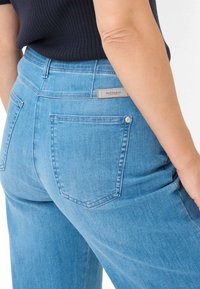  Lichtblauwe denim jeans met een relaxte pasvorm, voorzien van een achterzak en een grijs label met "Raphaela" in reliëf. Soepele textuur en casual ontwerp.