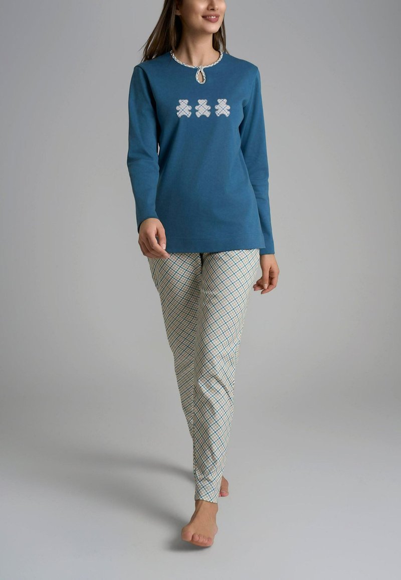 Maglietta blu a maniche lunghe con scollatura a chiave, con tre motivi geometrici bianchi; abbinata a pantaloni a quadri bianco e blu.