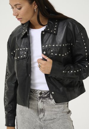 Sort læderjakke med sølvnitter, med krave, to frontlommer og en cropped fit, parret med lys grå denim.