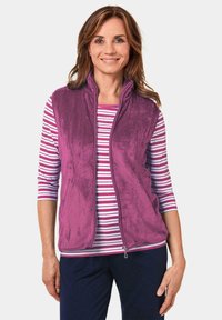 Fleece-Weste in Lila mit hohem Kragen und Reißverschluss, kombiniert mit einem weiß-pink gestreiften Shirt. Glatte Textur, lässiges Design.