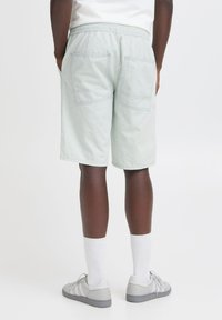 Pantaloni corti verde chiaro con cintura elastica, due tasche posteriori e vestibilità ampia. Il tessuto appare morbido con dettagli di cucitura visibili.