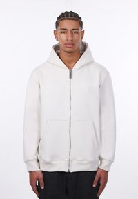 Svijetlosiva zip-up majica s kapuljačom napravljena od mekanog materijala, s prednjim džepom, rebrastim manžetama i izvezenim logotipom na lijevoj strani prsiju.