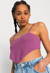 Top cropped de malha roxa com alças finas, apresentando um padrão texturizado e uma bainha assimétrica. Combinado com calções de ganga de cintura alta.