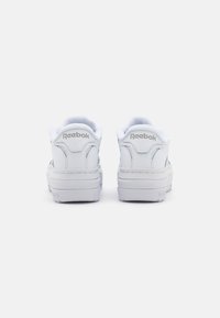 Bele Reebok športne copate iz gladkega usnja, nizkega dizajna, z oblazinjenimi ovratniki in embosiranimi logotipnimi akcenti na peti in strani.