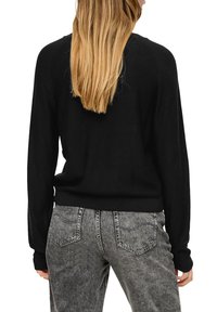 Schwarzer Strickpullover mit rundem Ausschnitt und langen Ärmeln, gerippter Saum, getragen mit grauen Jeans aus Denim mit Gesäßtaschen.