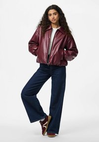 Burgundy faux läder bomberjacka med dragkedja fram, oversized passform och sidofickor, som är kombinerad med vida mörka jeans och burgundy sneakers.