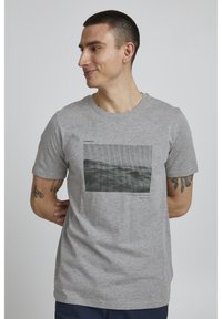 Camiseta de algodón gris con un gráfico monocromo rectangular de un paisaje, acompañado de texto en negro, de mangas cortas y cuello redondo.
