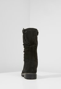 Botte noire en daim hauteur genou présentant un design débordant, des accents cousus et un détail de boucle sur le côté, avec une semelle en caoutchouc texturée.