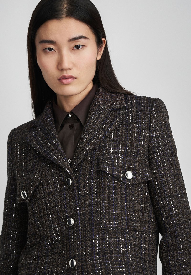 Pruunruutuline jakk hõbedase lõngaga, mis on kohandatud sobivusega, kahe eesmise tasku, krae ja läikivate hõbedaste nuppudega.