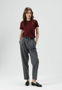 Bordeauxrode t-shirt met korte mouwen gecombineerd met grijze geplooide broek. De broek heeft een ruime snit en een zwarte riem. Zwarte loafers maken de outfit compleet.