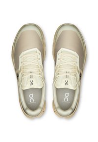 Jasnobeżowe buty sportowe z siateczkowym wierzchem, wzmocnionym czubkiem i gumową podeszwą. Zawierają sznurówki oraz logo na języku i wkładce.