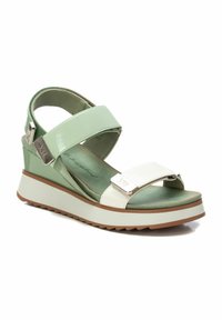 Sandal de cuña verde con correas blancas, plantilla texturizada y acentos de hardware plateado. Presenta una suela de goma con una capa contrastante.