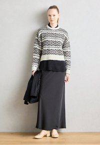 Stickad tröja med svart och vitt geometriskt mönster, lagd över en svart topp, ihop med en lång grå kjol och beiga klackskor med blockklack.
