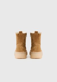 Bruine suède enkelboots met een gestikte zool, voorzien van een zachte binnenvoering en twee zijritsen voor gemakkelijke toegang.