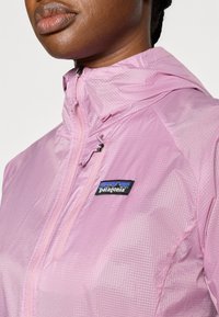 Ανοιχτό ροζ μπουφάν Patagonia με υφή στην επιφάνεια, διαθέτει εμπρόσθιο φερμουάρ και κουκούλα. Περιλαμβάνει χαρακτηριστικό λογότυπο στο στήθος.