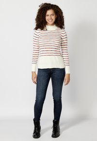 Maglione lavorato a maglia con colletto alto, base color crema con strisce orizzontali multicolori. Abbinato a jeans slim scuri e stivali neri con lacci.