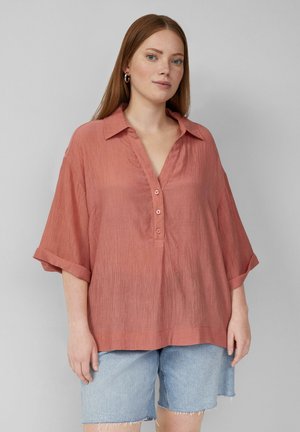 Salmon-colored, textured blouse with a collar, button placket, and rolled short sleeves, paired with denim shorts.