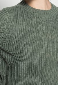 Grüner gestrickter Pullover mit gerippter Textur, rundem Halsausschnitt und langen Ärmeln, aus einem weichen, wollähnlichen Material.