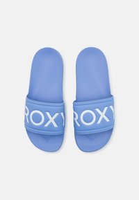 Modré gumové šľapky so širokým popruhom, na ktorom je biele logo "ROXY". Povrch má miernu textúru a podrážky sú ploché.