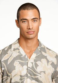 Camisa de manga corta y cuello en gris con grandes estampados florales blancos, con una textura suave y cierre de botones.