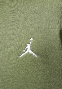 Groene katoenstof met een gladde textuur heeft een witte geborduurde Jumpman-logo, gepositioneerd aan de linkerkant.