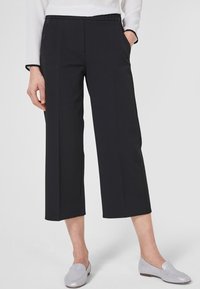 Černé zkrácené kalhoty s lehkým materiálem, širokým střihem nohavic, bočními kapsami a elastickým pasem. Spárováno se světle šedými botami.