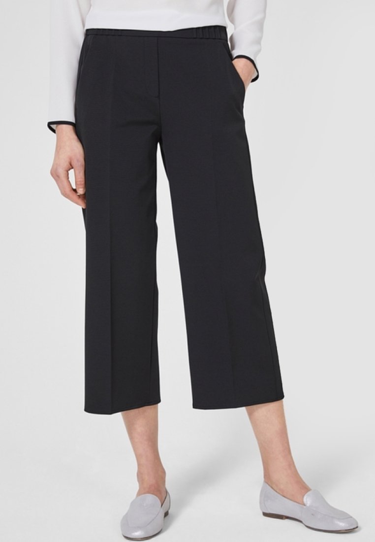 Černé zkrácené kalhoty s lehkým materiálem, širokým střihem nohavic, bočními kapsami a elastickým pasem. Spárováno se světle šedými botami.