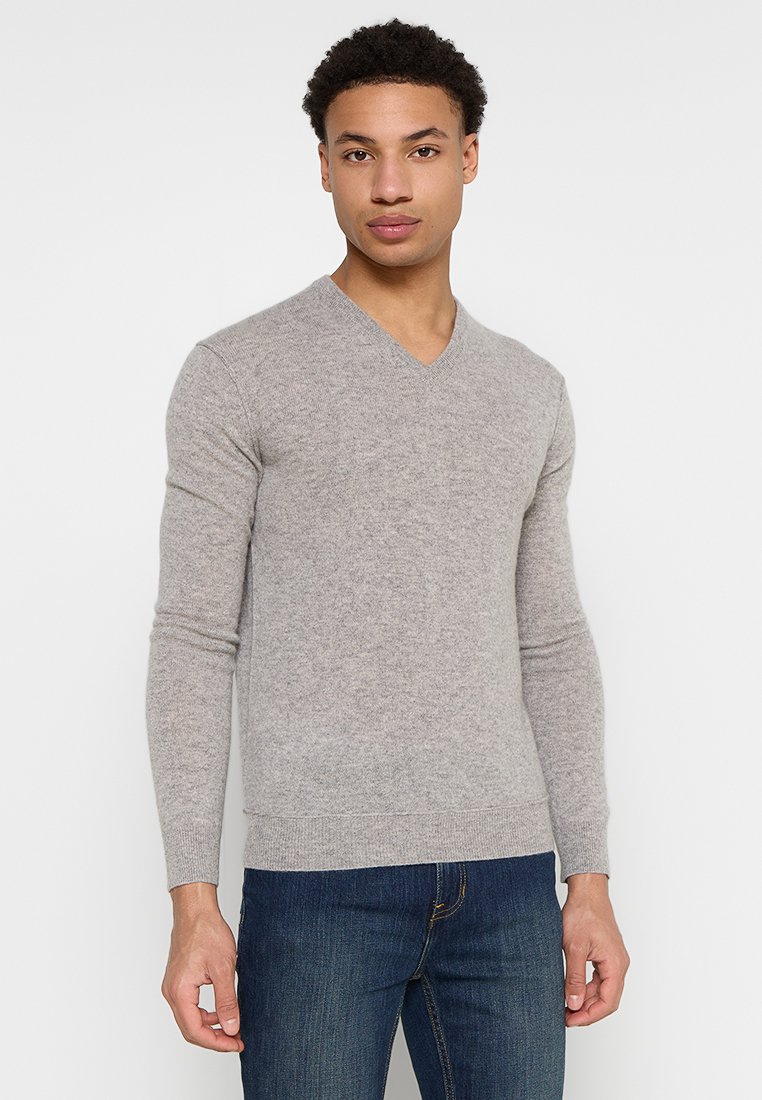 Grauer V-Ausschnitt-Pullover aus weichem Material mit langen Ärmeln und geripptem Saum, kombiniert mit dunkelblauen Jeans. Einfaches und tailliertes Design.