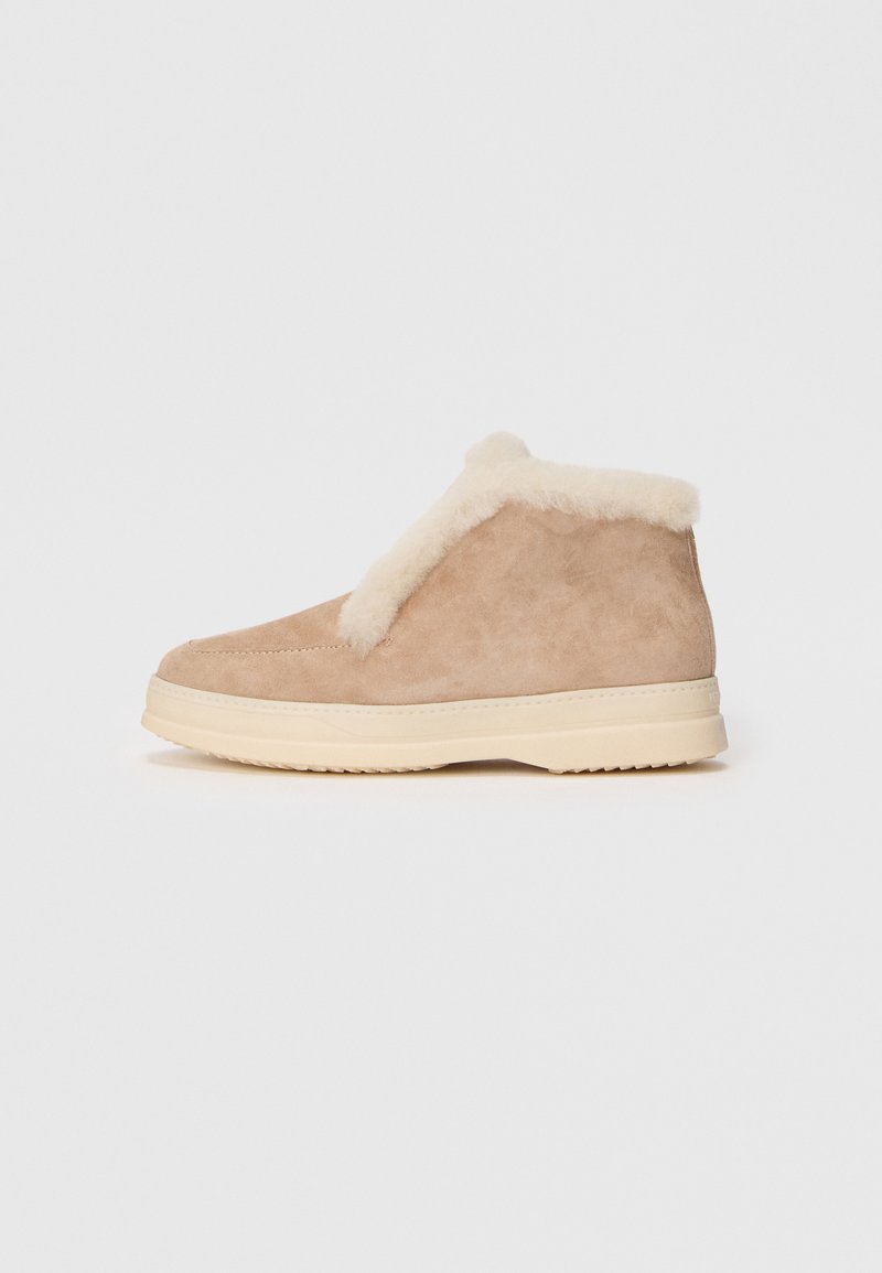 Beige suede ankle boot with cream-colored faux fur lining and a thick off-white rubber sole, shown from the side on a white background.