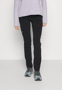Pantalones de exterior negros con un diseño ajustado, bolsillo lateral sutil y combinados con zapatillas deportivas grises. La parte superior es una camisa de manga larga de color púrpura claro.