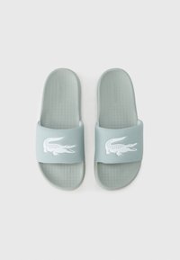 Σαγιονάρες Lacoste σε ανοιχτό πράσινο με υφασμένο πέλμα και σταθερό λουράκι που φέρει λευκό λογότυπο κροκόδειλου.