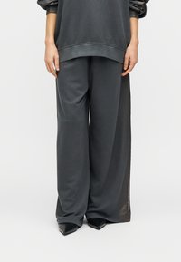 Σκούρο γκρι φαρδιά φούτερ και παντελόνι με ευρύ πόδι από μαλακό ύφασμα. Διαθέτει ριμπ μανσέτες και γυαλιστερές λεπτομέρειες στις πλευρικές επιφάνειες.