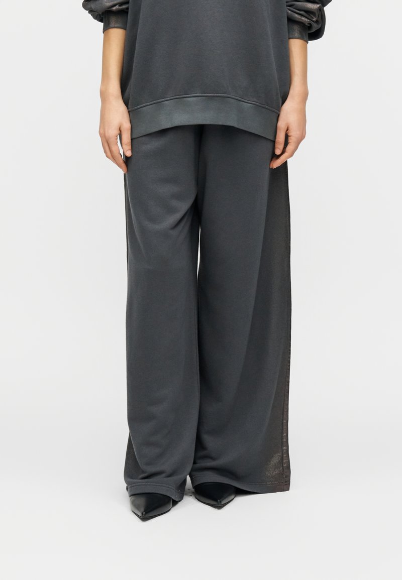 Σκούρο γκρι φαρδιά φούτερ και παντελόνι με ευρύ πόδι από μαλακό ύφασμα. Διαθέτει ριμπ μανσέτες και γυαλιστερές λεπτομέρειες στις πλευρικές επιφάνειες.