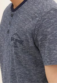 Tmavě modrá texturovaná košile s krátkým rukávem, s knoflíkovým výstřihem henley a vyšitým logem na hrudi.