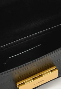 Schwarze Handtasche aus strukturiertem Leder mit einem goldfarbenen Metallschloss. Das Innenfutter besteht aus weichem schwarzem Stoff und verfügt über einen Kartensteckplatz zur besseren Organisation.