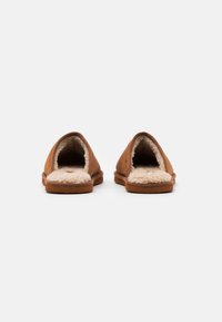 Brune semskede tøfler uden hæl med blød beige pelsforing og gummisål, der har et åbent bagdesign for nem påtagning.