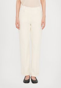 Cream-colored trousers with a straight cut, featuring a high waist, rolled cuffs, and side pockets. Paired with black flats.