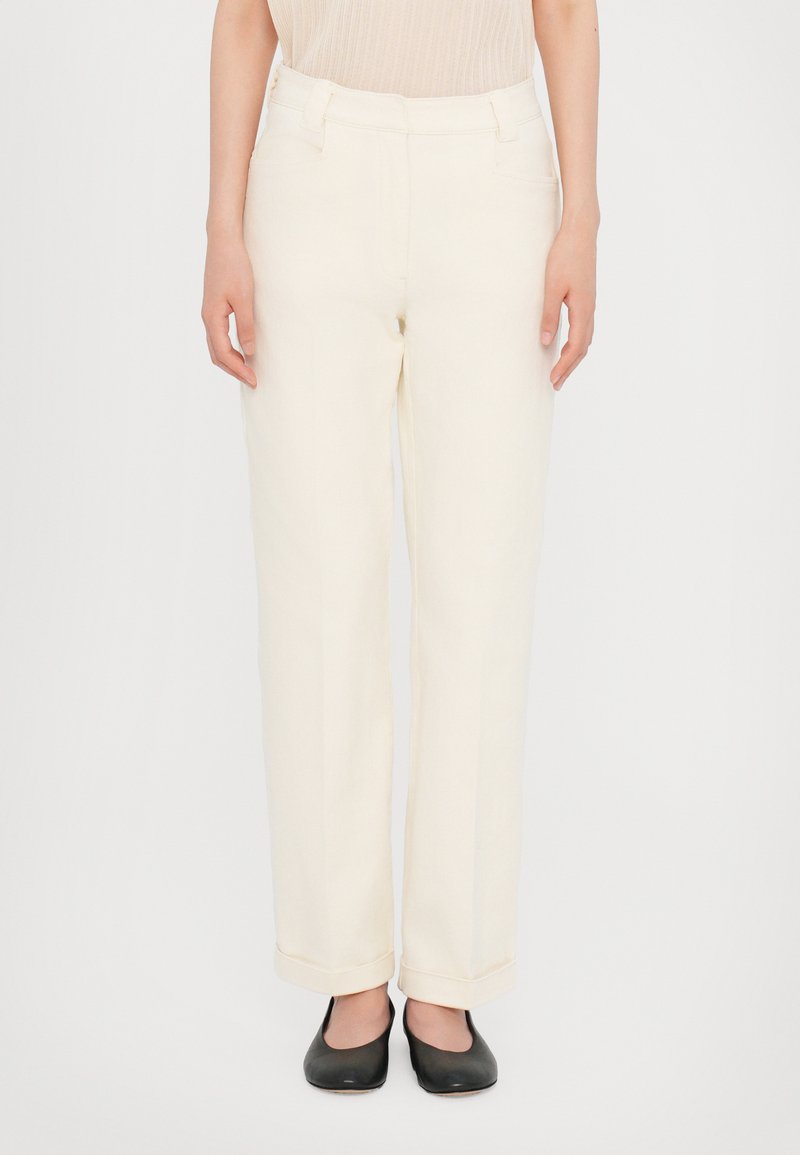 Cream-colored trousers with a straight cut, featuring a high waist, rolled cuffs, and side pockets. Paired with black flats.