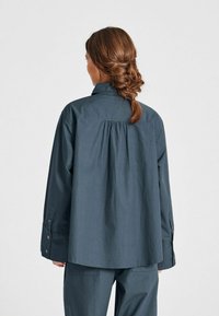 Camicia blu scuro a maniche lunghe con colletto e dettaglio arricciato sul retro, realizzata in un tessuto leggero con polsini con bottoni.