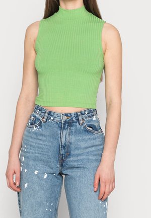 Top corto verde de canalé con cuello alto. Combinado con jeans de tiro alto azules que tienen detalles de manchas de pintura.