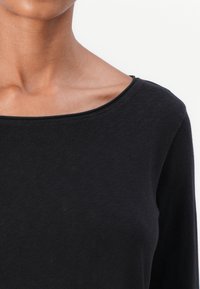 Svart långärmad topp med vid halsringning, tillverkad av mjukt, texturerat tyg. Designen har en figurnära silhuett och subtil stretch.