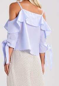 Světle modrá pruhovaná blůza s odhalenými rameny, volánkovými detaily a zavazovacími rukávy, kombinovaná s krémovou sukní s puntíky.