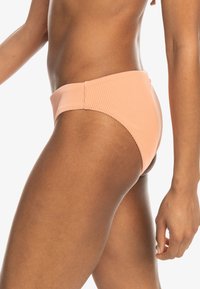 Brosky bikini spodok v broskyňovej farbe s vysokým pásom. Má hladkú textúru a minimalistický dizajn, ktorý zvýrazňuje pás.