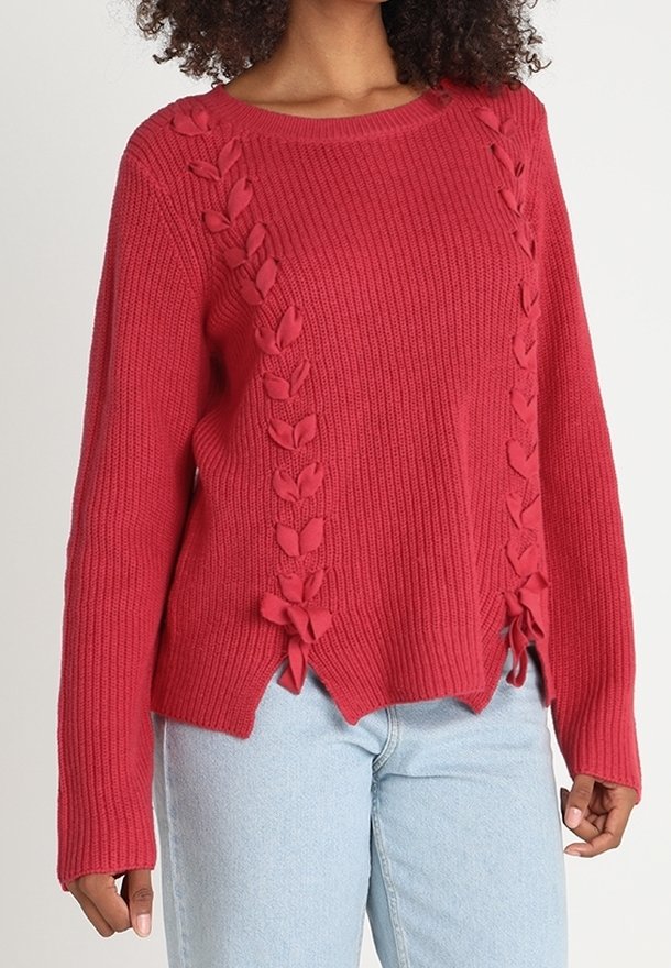 Punainen neulottu villapaita, jossa on resorikuviointi, lehtimuotoisia yksityiskohtia ja nyörit sivuilla, ja hieman väljä istuvuus.