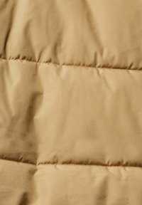 Tessuto di giacca a vento in un colore beige chiaro, caratterizzato da una superficie liscia con linee di cucitura orizzontali che creano un motivo trapuntato.