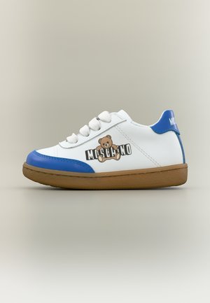 Zapatilla para niño blanca y azul con suela marrón, logo de oso de peluche en estilo caricatura y la marca "Moschino" en el lateral y la lengüeta del talón.