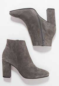 Bottes chevilles en daim gris avec un bout pointu et un talon épais. Elles disposent d'une fermeture éclair latérale et d'une texture lisse avec des coutures contrastantes.