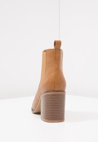 Botín de cuero marrón claro con punta redondeada, paneles laterales elásticos y un tacón apilado texturizado. Cuenta con una lengüeta en la parte posterior para facilitar su uso.